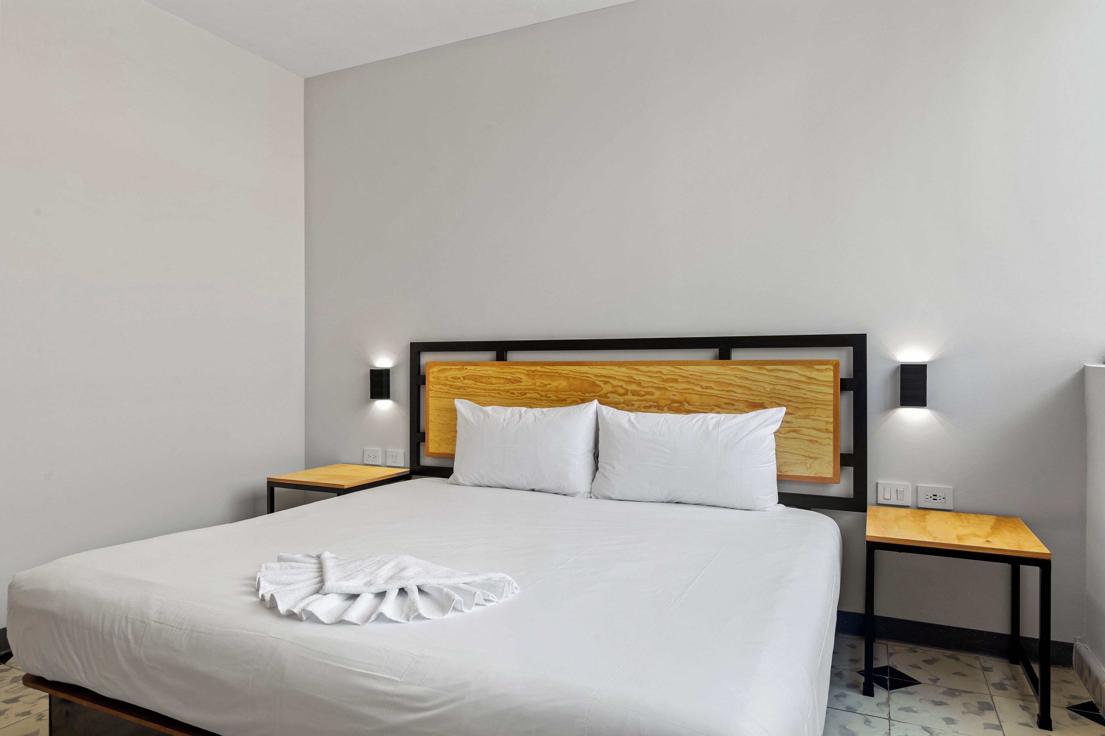 Habitación de hotel con una cama, dos mesitas de noche y cabecera con iluminación integrada.
