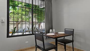 Un comedor con una mesa dispuesta para dos personas, sillas, una ventana con vistas a zonas verdes y una cortina.