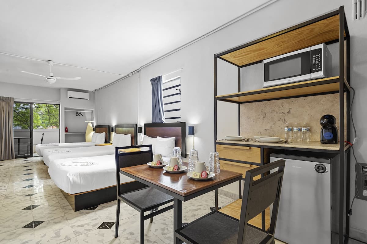 A hotel room with a bed, a desk with a microwave, a refrigerator, and a window with curtains.