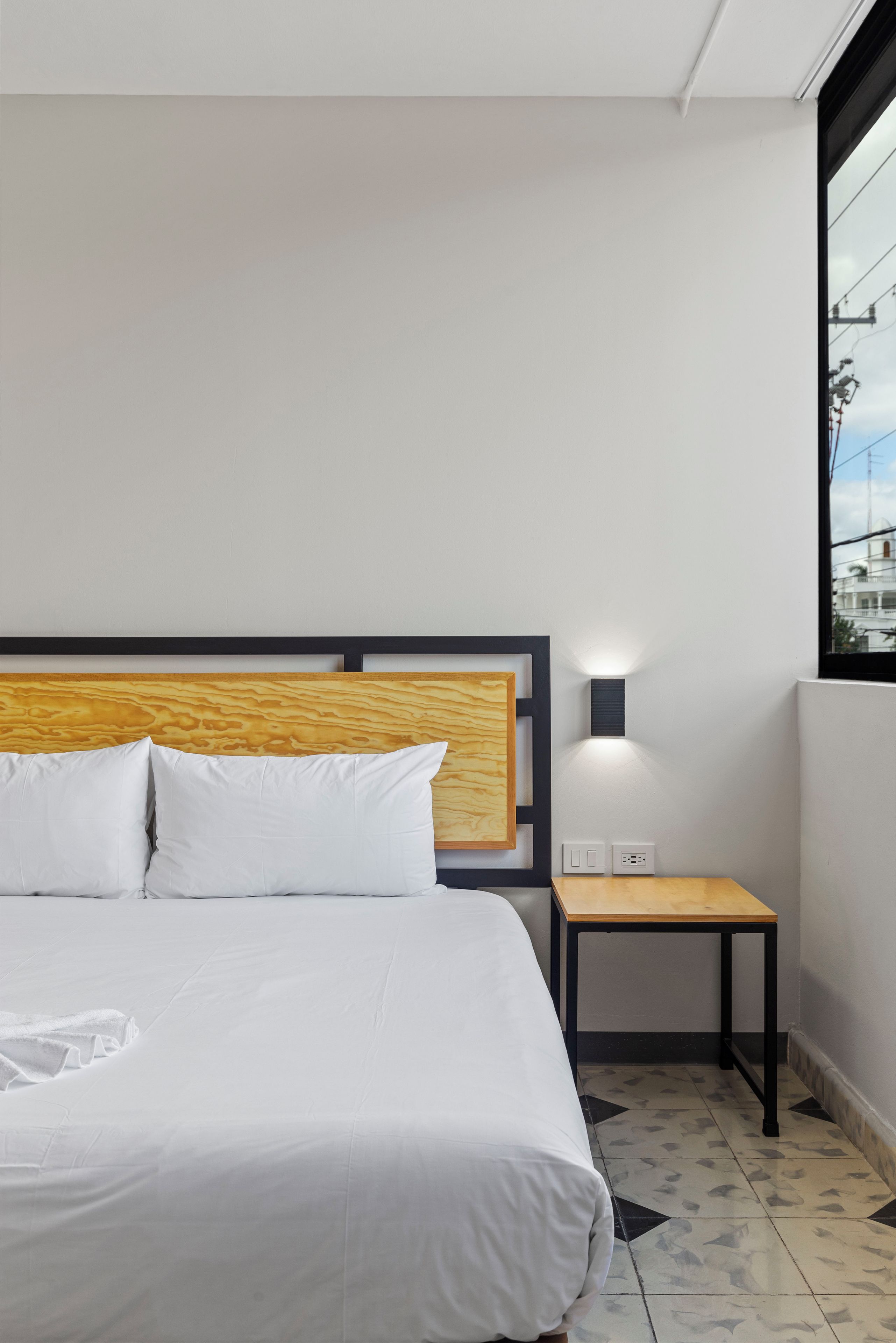 A hotel room with a large bed, a wooden headboard, a small table, and a wall-mounted light.