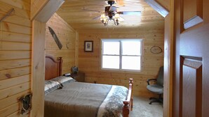 A wooden cabin bedroom with a bed, a ceiling fan, a window, and a chair. - Quiet, Cozy Paoli Cabin Overlooking a Nice Pond (Paoli)