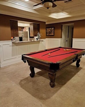 Enjoy a game of pool in this spacious room, featuring a kitchen area and ceiling fan.