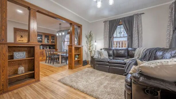 Una sala de estar acogedora con un sofá de cuero, estanterías de madera, una zona de comedor y un amplio ventanal con cortinas.