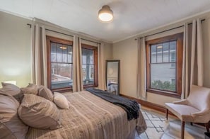 Relax in a serene bedroom with a large bed, two windows, and a comfortable chair.