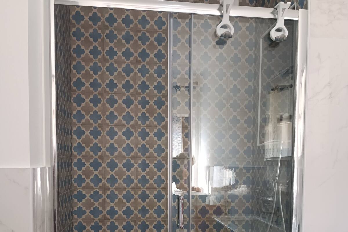 A glass-enclosed shower with a patterned tile wall.