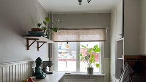 Een compacte keuken met een inbouwfornuis, een raam met uitzicht op de straat en een kleine Boeddhabeeld op het aanrecht.