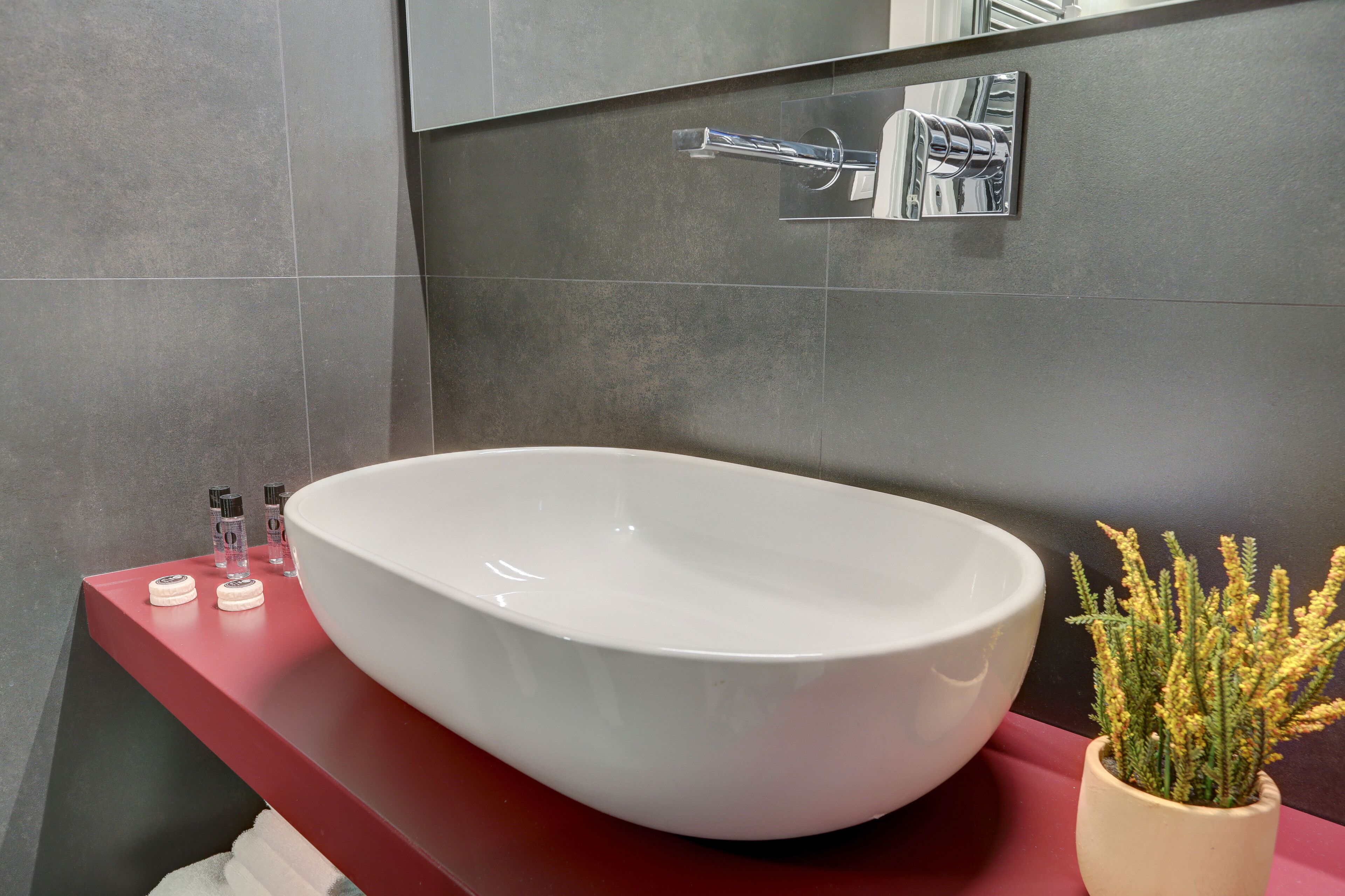A modern bathroom with a white vessel sink, a red countertop, and a small potted plant.