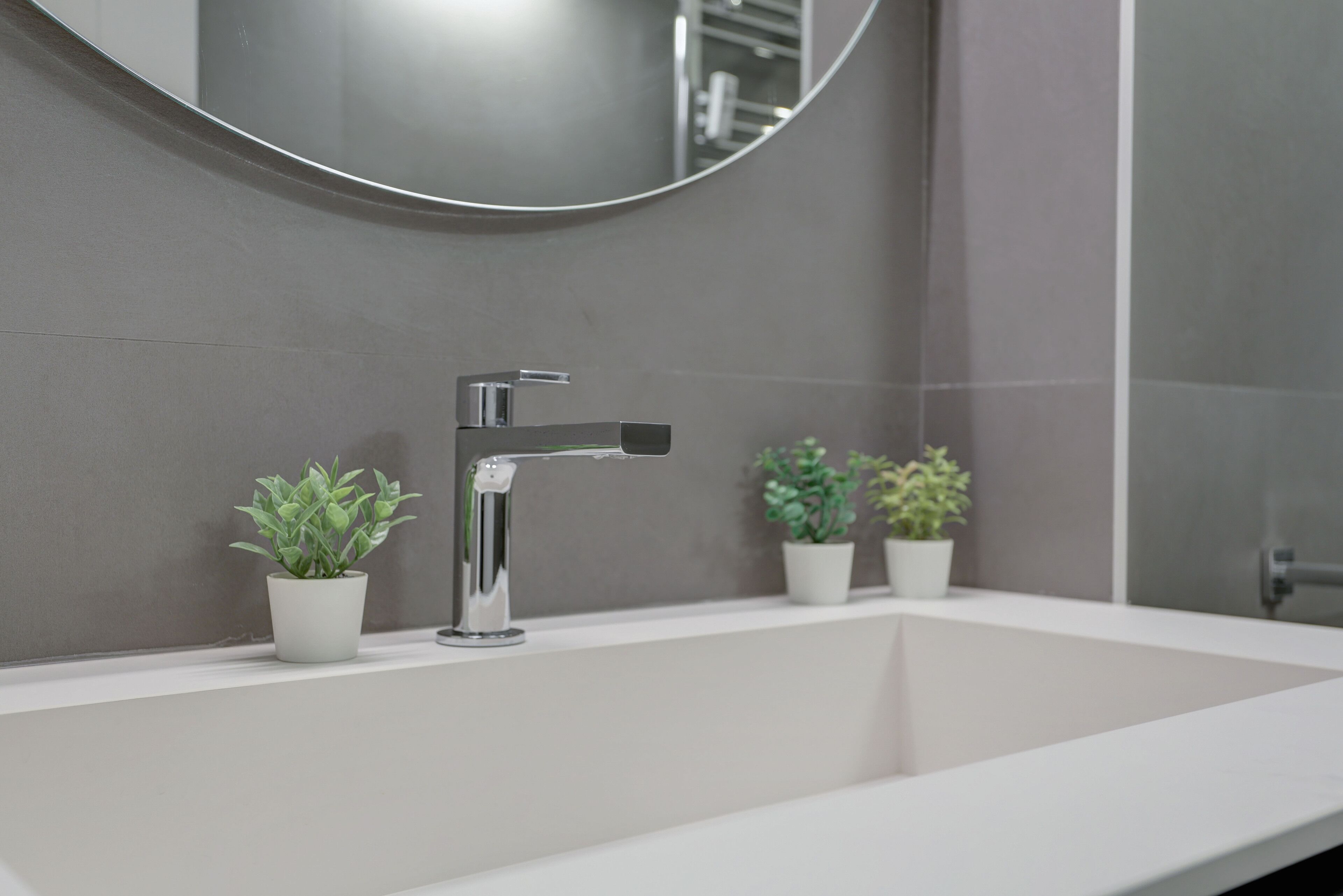 A modern bathroom with a white sink, chrome faucet, and three potted plants.