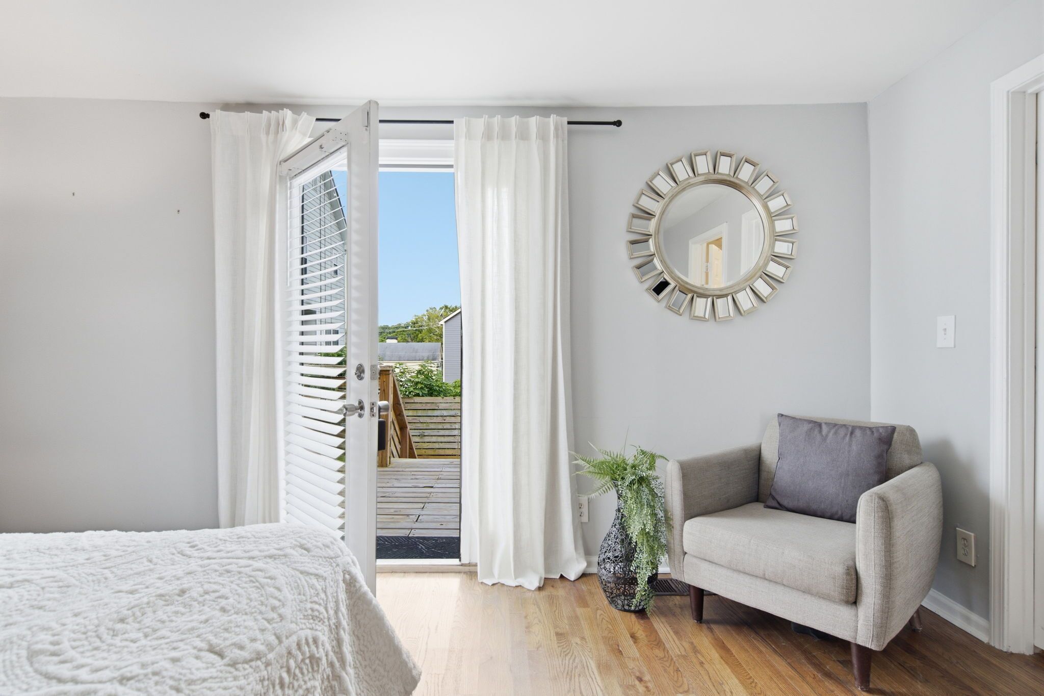 A bedroom with a bed, a chair, a potted plant, and a view of a balcony.