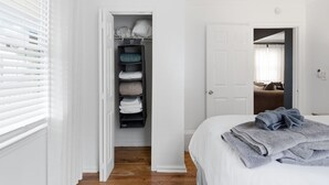 A bedroom with a bed, a closet with folded clothes, and a door leading to another room. - NEW! 3 Br Home Steps away from Stadium & Downtown! (Atlanta)