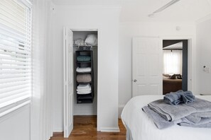A bedroom with a bed, a closet with folded clothes, and a door leading to another room. - NEW! 3 Br Home Steps away from Stadium & Downtown! (Atlanta)