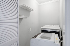 Une buanderie équipée d’un lave-linge et d’un sèche-linge à chargement frontal, d’une étagère au-dessus du sèche-linge et d’une prise électrique fixée au mur.