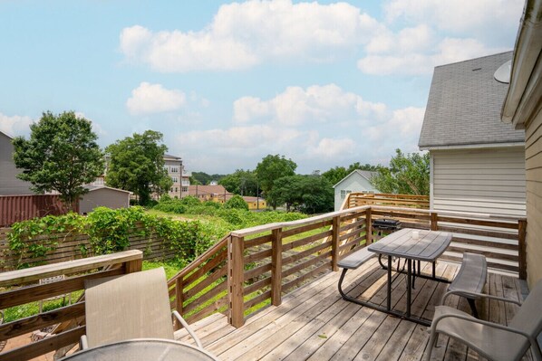A wooden deck with a table and chairs, surrounded by a wooden fence and greenery.