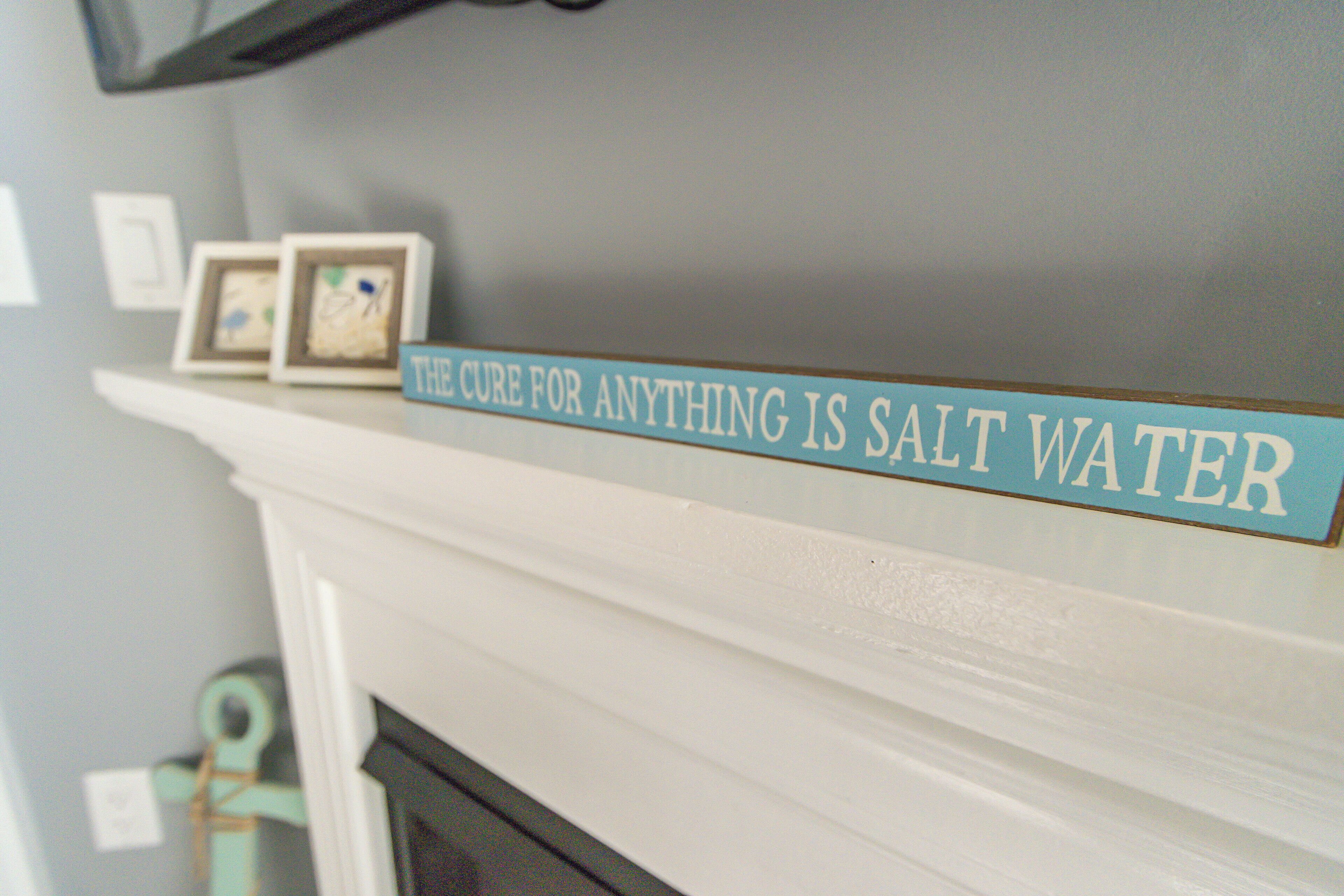 A fireplace mantel with a sign that reads "The cure for anything is salt water."