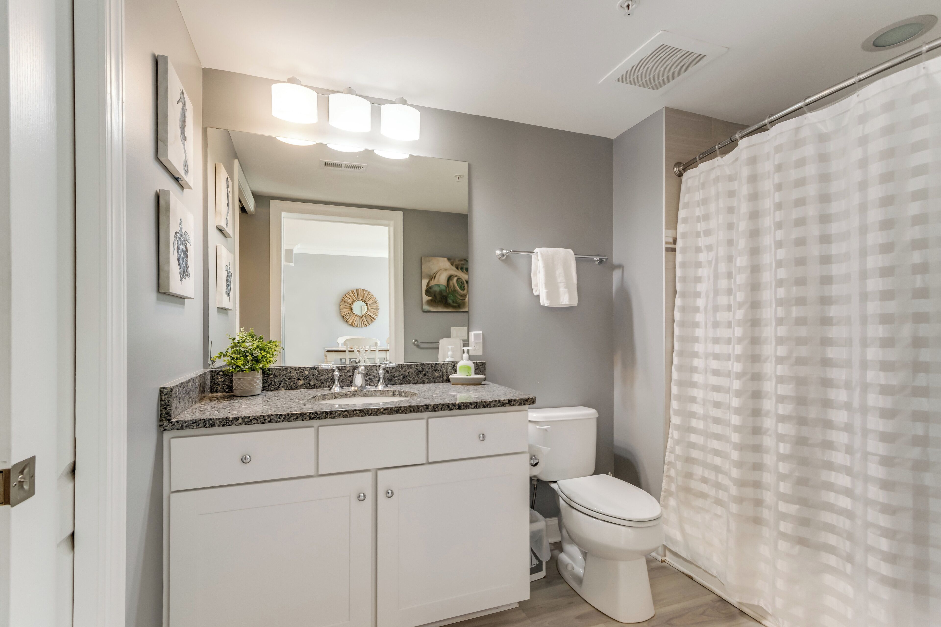 A modern bathroom with a white toilet, a granite countertop, a sink, and a shower curtain.