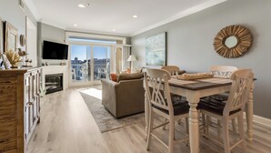 A modern living room with a dining area, a fireplace, and a large window offering a city view. - Lovely Two Bedroom Condo with Stunning Bay Views (Dewey Beach)