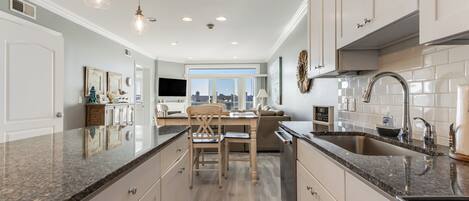 A modern kitchen with granite countertops, stainless steel appliances, and a large window offering a city view.