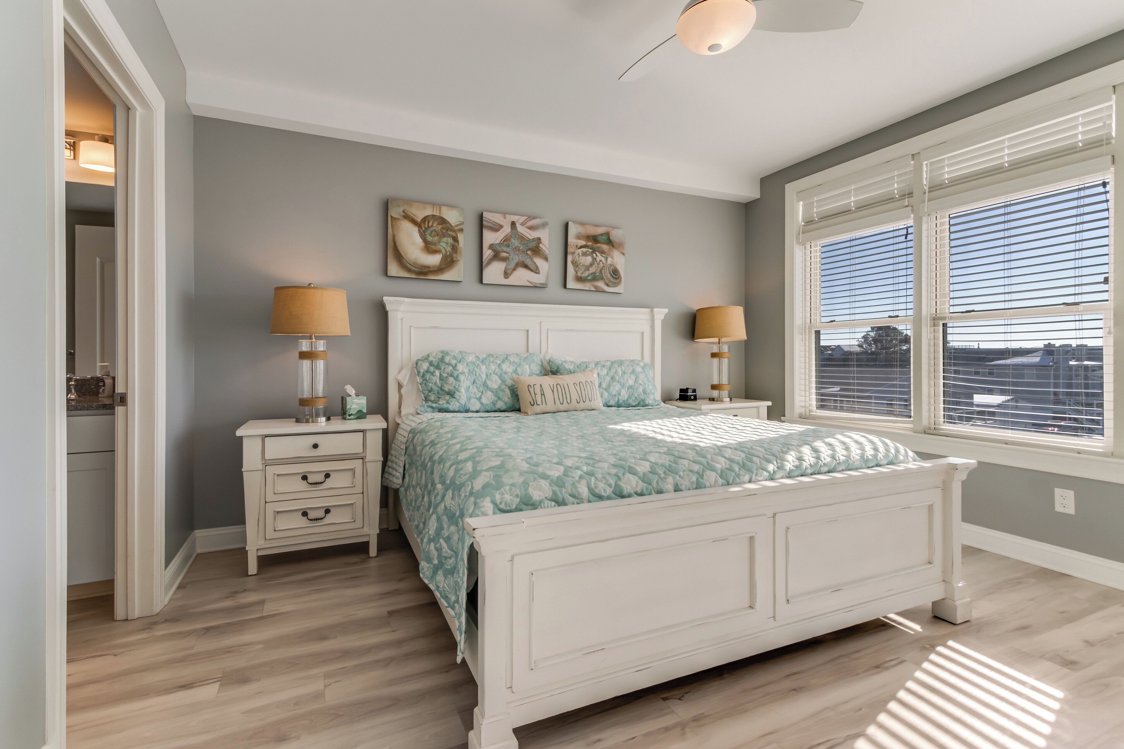 A bedroom with a bed, two bedside tables, a nightstand, a window with blinds, and wall art.