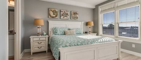 A bedroom with a bed, two bedside tables, a nightstand, a window with blinds, and wall art.
