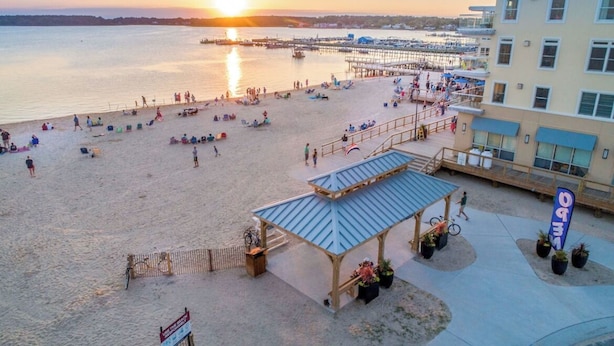 A beach with a gazebo, a pier, and a building with a blue awning. - Lovely Two Bedroom Condo with Stunning Bay Views (Dewey Beach)
