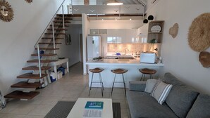Uma sala de estar moderna com um sofá cinzento, uma mesa de centro branca e uma escadaria que leva a um andar superior.