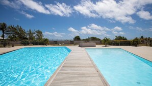 Piscina com um deck de madeira, cercada por uma grade e palmeiras.