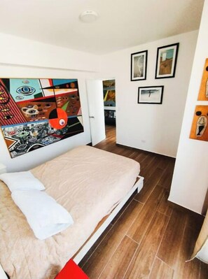 Ein Schlafzimmer mit einem Bett, einer Tür zu einem Flur und einer Wand mit gerahmten Bildern.