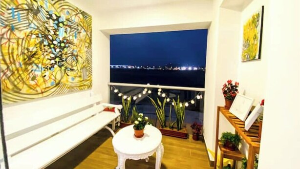 A room with a view of a cityscape at night, a large abstract painting on the wall, a small round table with a plant, and a wooden bench. - Beach Apartment /Gallery in Punta Hermosa (Lima)