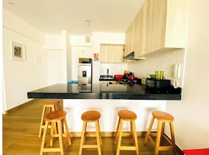 A modern kitchen with a black countertop, wooden stools, and a central island. - Beach Apartment /Gallery in Punta Hermosa (Lima)