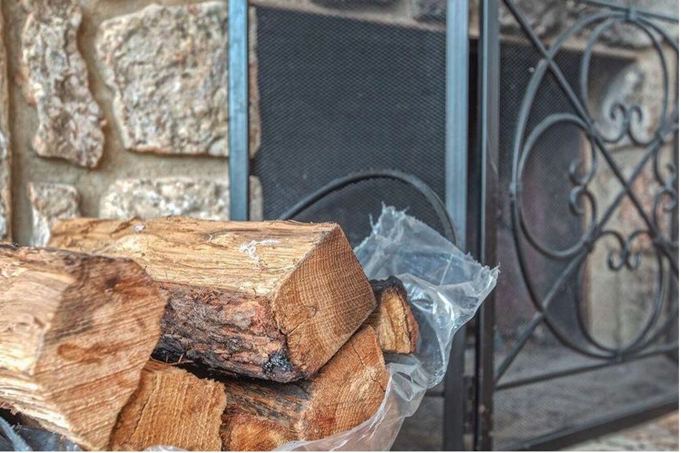 Un montón de leña en una bolsa de plástico, junto a un muro de piedra y una reja de metal.