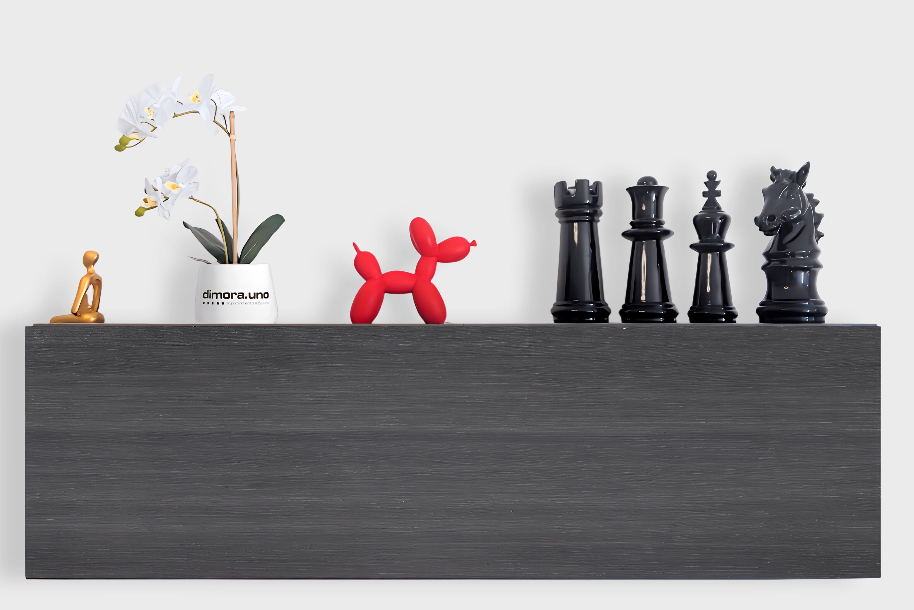 A shelf with a potted orchid, a red balloon sculpture, and black chess pieces.