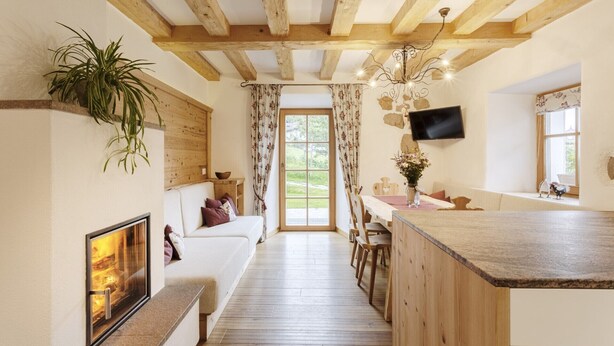 A cozy room with a fireplace, wooden beams, a dining area, and a TV mounted on the wall. - Centrally located, family-friendly apartment in the middle of the Dolomites (Sankt Ulrich)