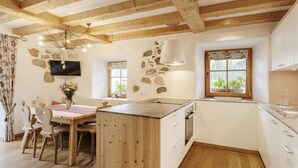 A rustic kitchen with wooden beams, a stone wall, and a dining area with a wooden table and chairs. - Centrally located, family-friendly apartment in the middle of the Dolomites (Sankt Ulrich)
