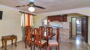 A dining area with a wooden table and chairs, a ceiling fan, and a kitchen with stone backsplash and wooden cabinets. - Tropical Paradise Retreat in Santo Domingo (Santo Domingo Este)