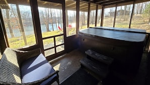 Un espacio de estar al aire libre cubierto con jacuzzi, mobiliario de mimbre y grandes ventanales con vistas a un paisaje natural.