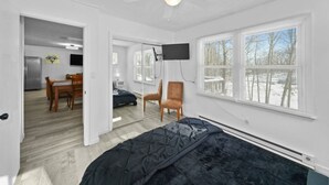 Un dormitorio con una cama, ventilador de techo, televisor y ventana con persianas.