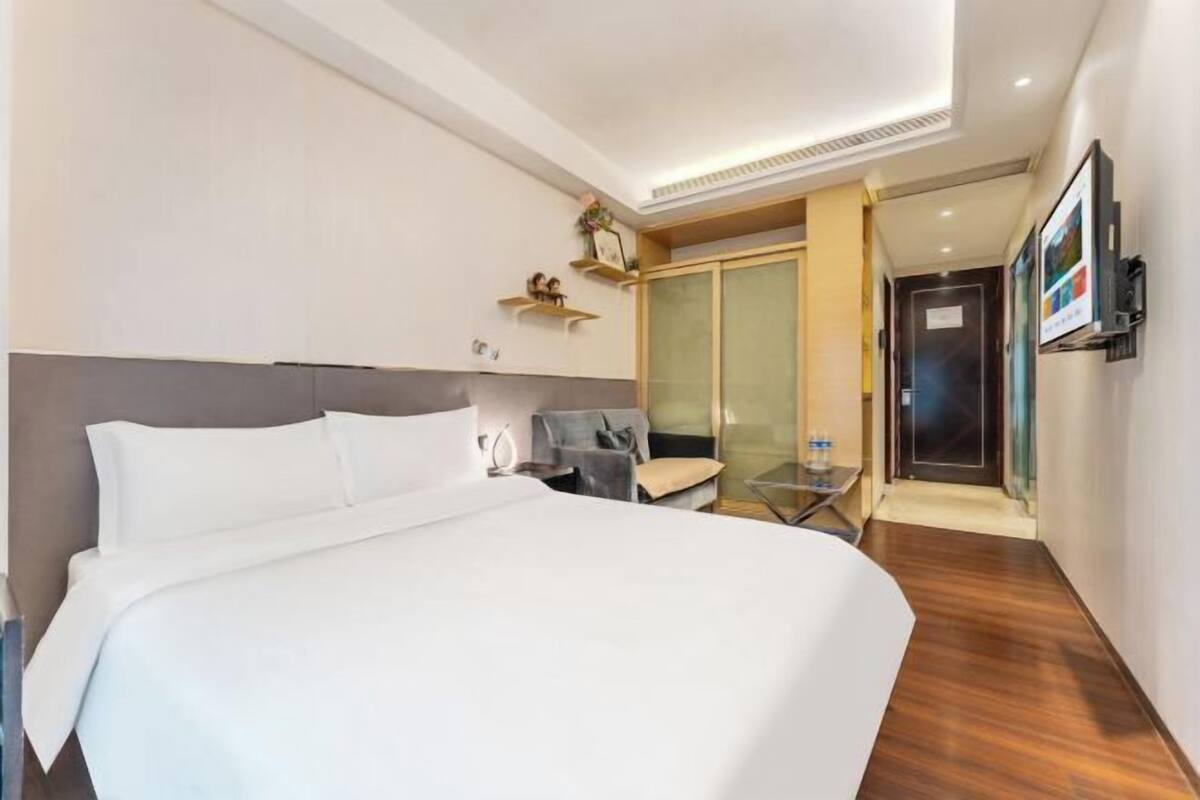 Une chambre d’hôtel moderne dotée d’un grand lit, d’un coin salon avec une chaise et une table, d’une armoire et d’un téléviseur fixé au mur.