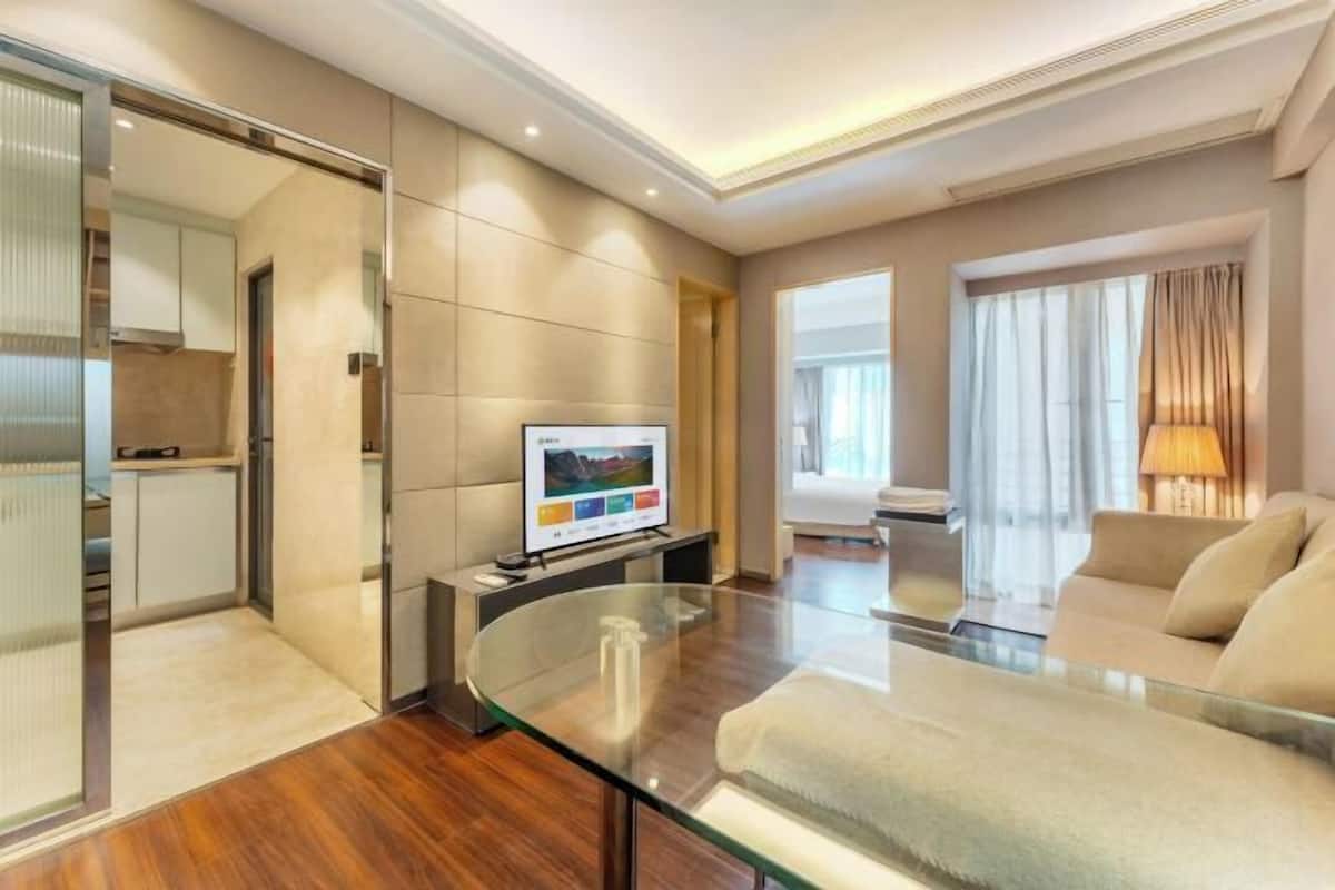 Une chambre d’hôtel moderne avec une table basse en verre, un canapé, un téléviseur à écran plat et un coin cuisine.