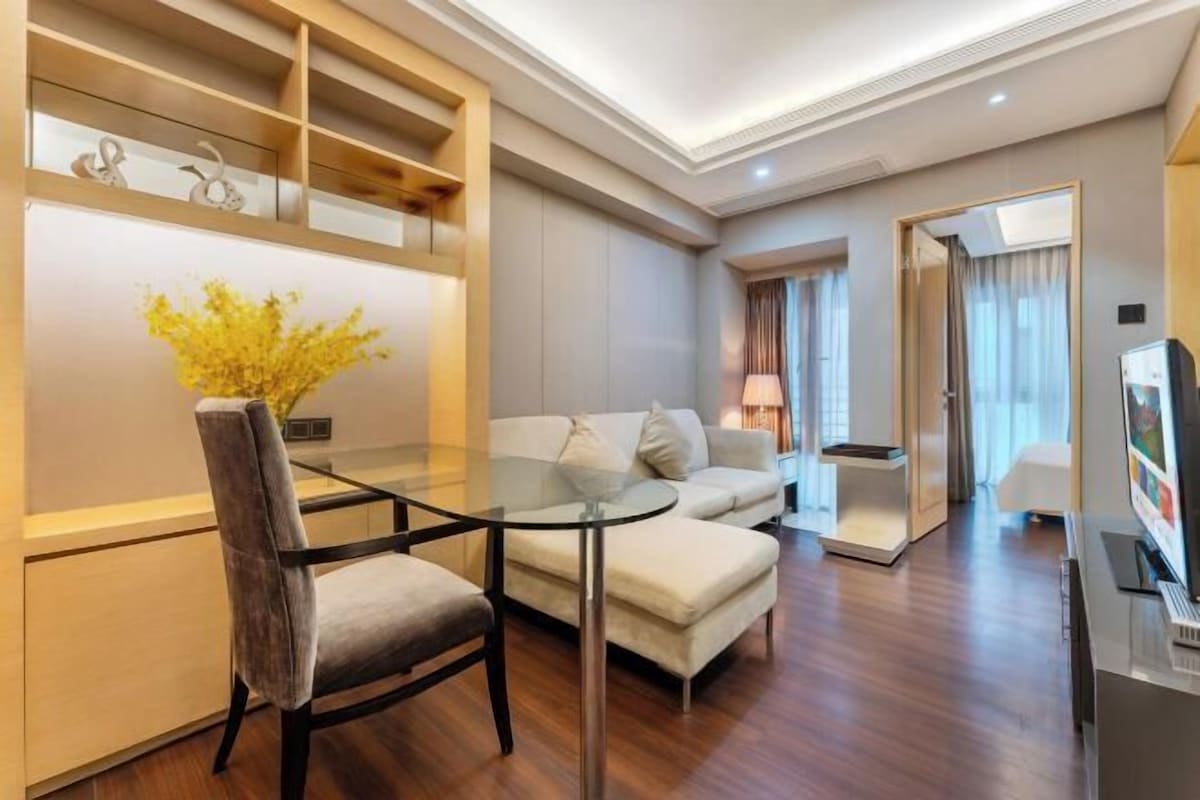 A modern living room with a glass-top dining table, a sofa, and a TV.