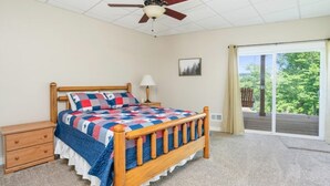 A bedroom with a wooden bed, a nightstand, a ceiling fan, a window with a view of greenery, and a sliding glass door.