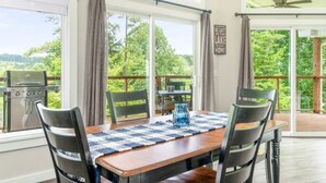 A dining area with a table set for four, large windows, and a view of greenery outside.