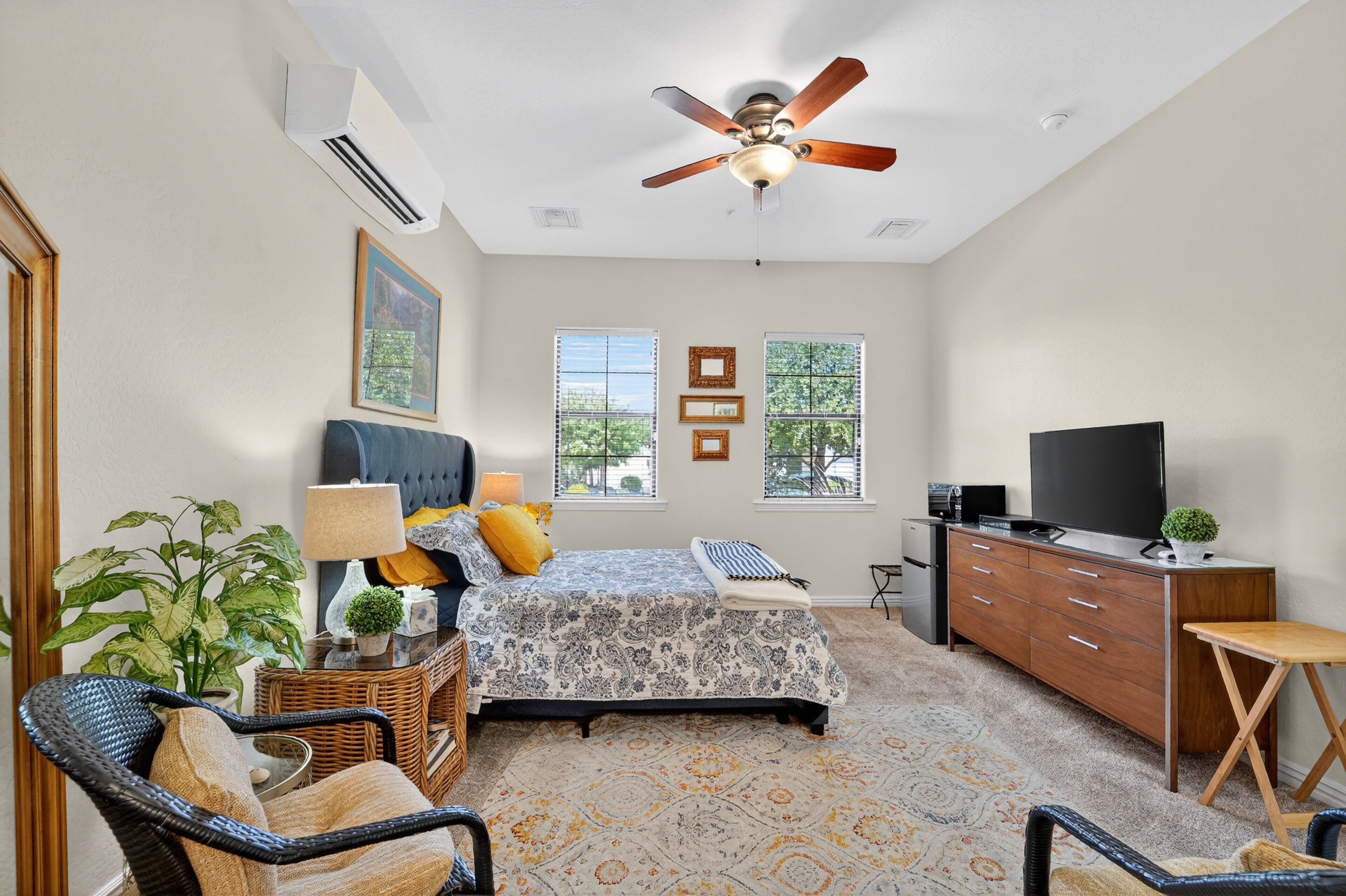 A bedroom with a bed, dresser, TV, and a ceiling fan.