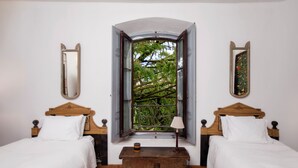 A bedroom with two wooden beds, a small table, and a window with a view of trees.