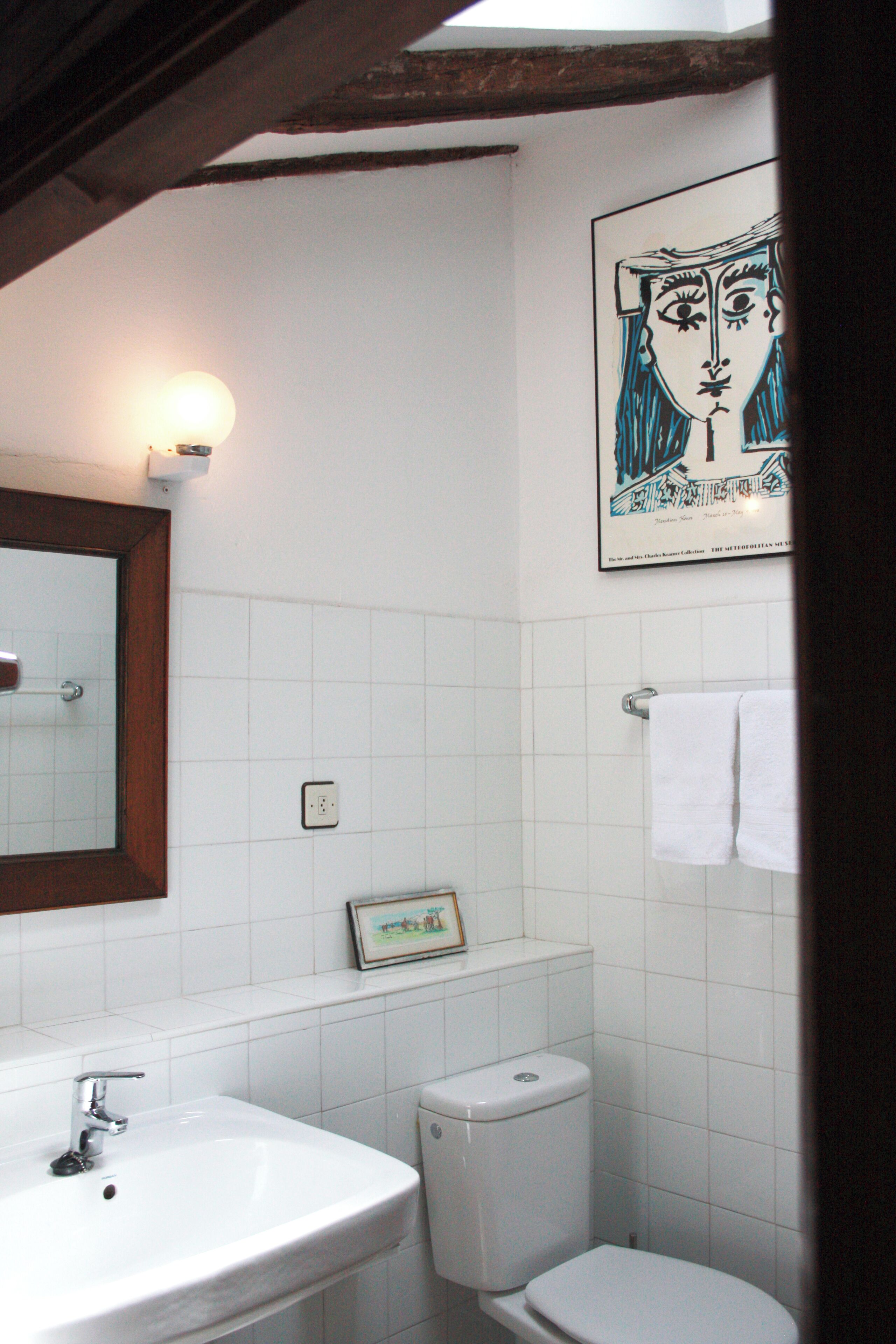 A bathroom with white tiles, a sink, a toilet, and a framed picture on the wall.