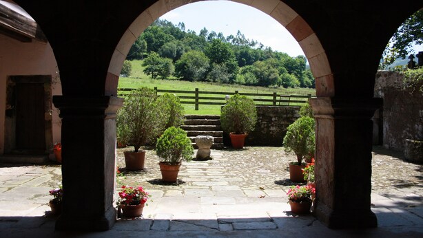 An arched entrance with potted plants and a stone pathway leading to a green field.