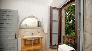 A bathroom with a wooden vanity, a large mirror, and a view through an open door to a balcony.