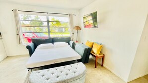A bedroom with a bed, a grey ottoman, a grey sofa, a small wooden table, and a TV on the wall. - Fun Kids Family Stay - FLL Cruise Guests & Airport! AirHockey-Arcade-Pool-Toys (Hollywood)