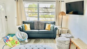 A living room with a grey sofa, colorful child seat, grey ottoman, patterned ottoman, and a bench. - Fun Kids Family Stay - FLL Cruise Guests & Airport! AirHockey-Arcade-Pool-Toys (Hollywood)