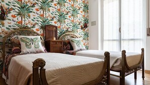 Een slaapkamer met twee houten bedden, bloemenbehang en een raam met dunne gordijnen.