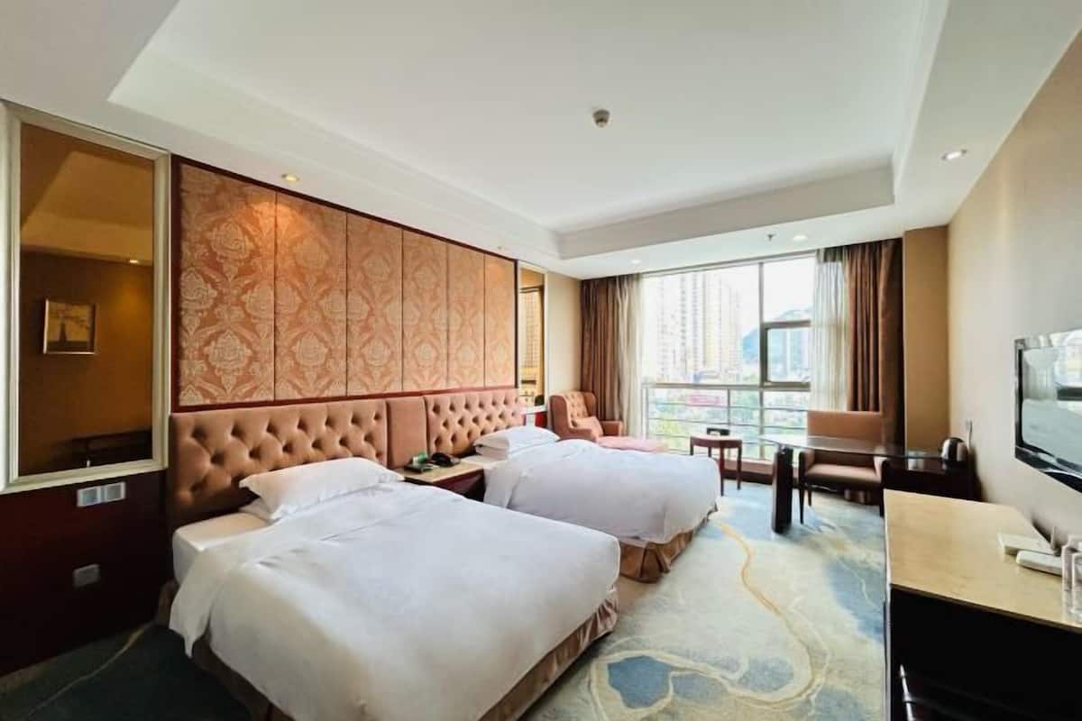 Een hotelkamer met twee bedden, een groot raam met gordijnen, een televisie en een bureau met stoel.
